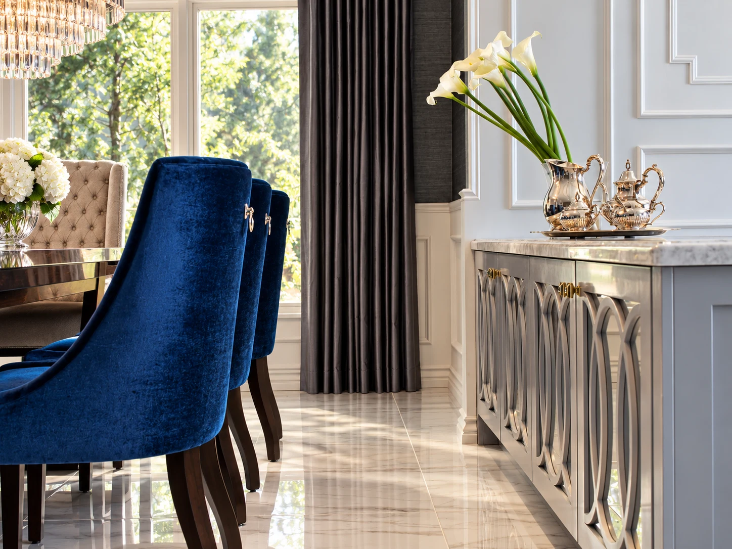 Blue velvet dining chair, patterned wall paneling, and flowers in natural light